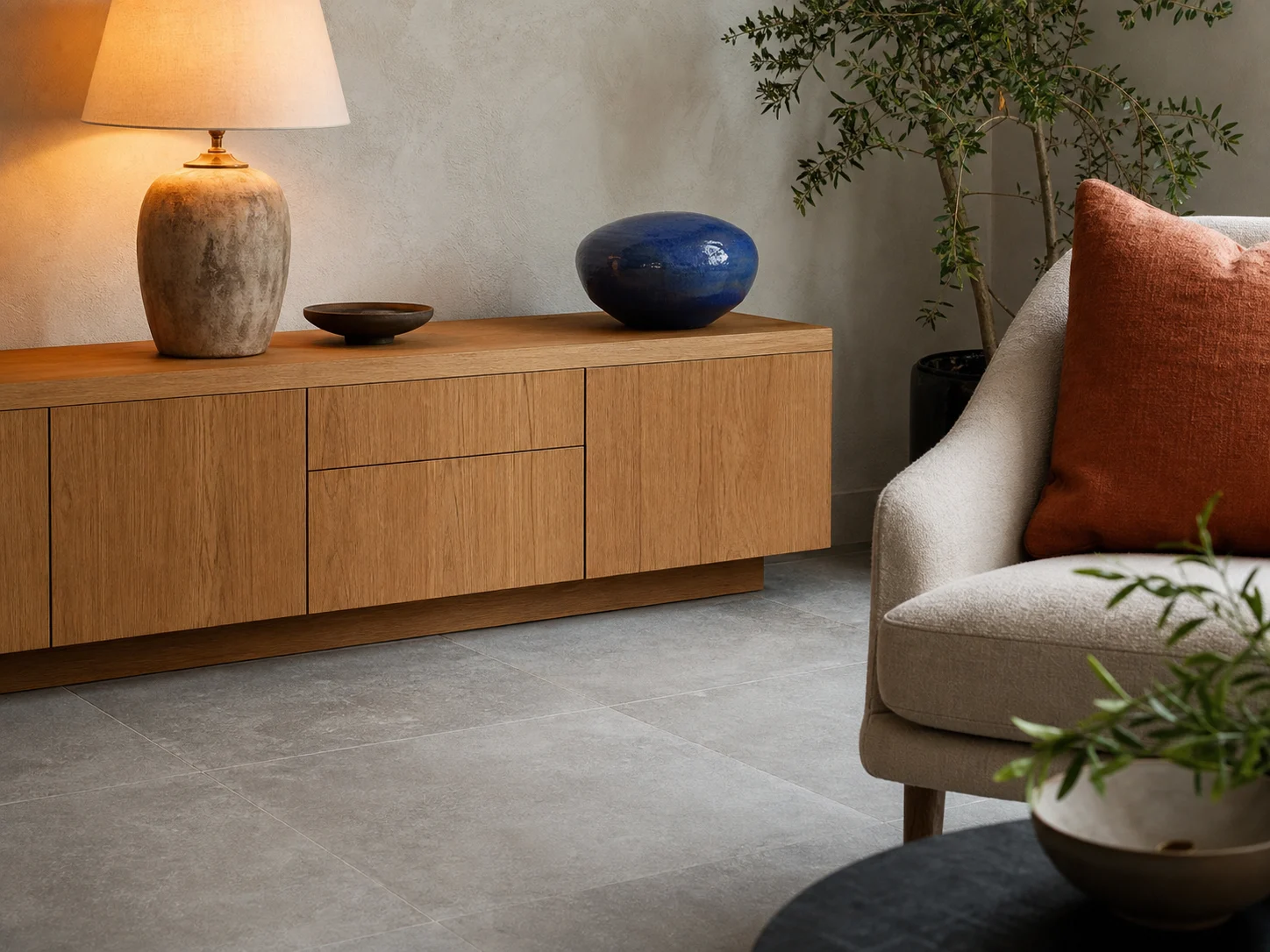 Coin salon avec carrelage gris, meuble bas en bois, lampe chaude et accents terracotta